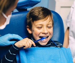 little boy brushing his teeth in dental chair smiling