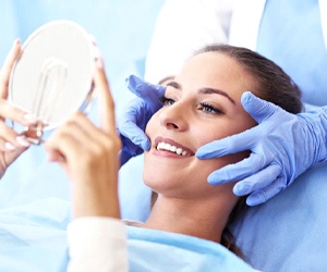 woman sitting in dental chair admiring her smile in handheld mirror