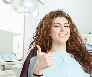 woman with curly hair giving a thumbs-up in the dental chair 
