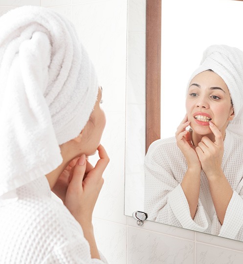 Woman in white robe looking at gums in reflection