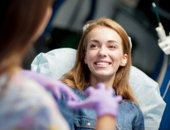 patient smiling at team member while laying in dental chair in Plano