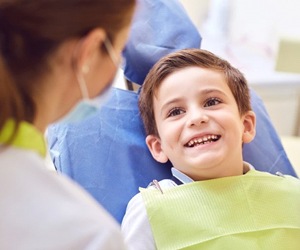 little boy sitting in dental chair smiling at dentist