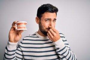 Man holding dentures and plugging his nose